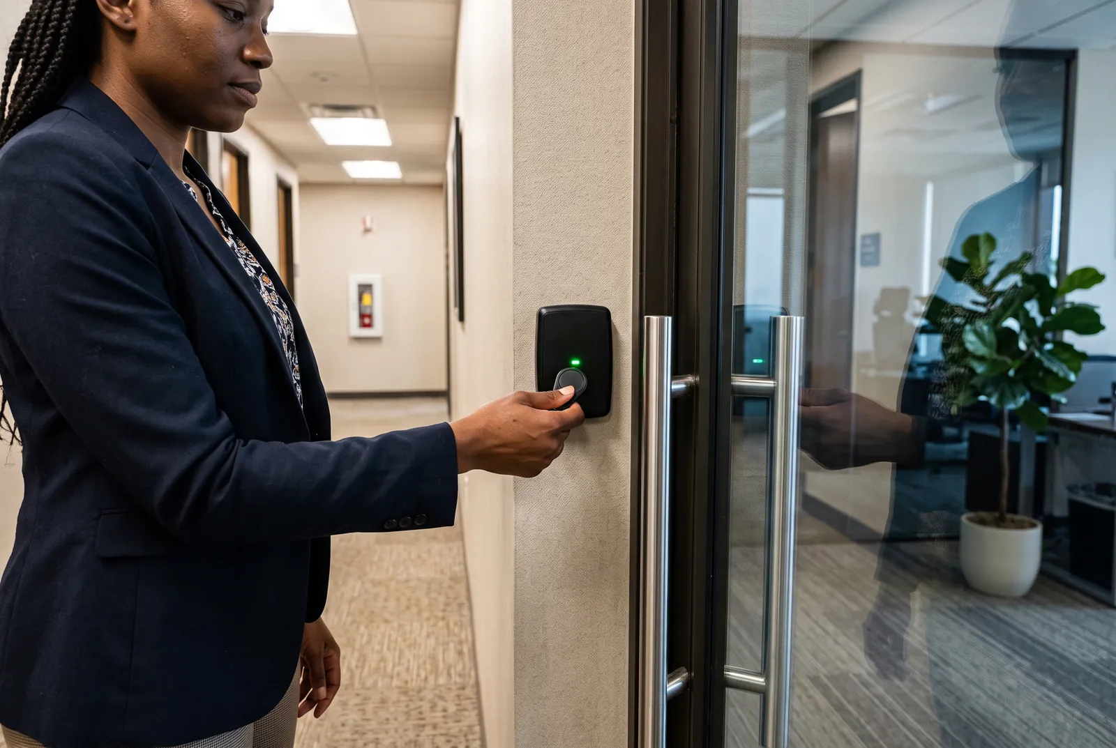An employee taps a key fob on a reader beside a glass office door.